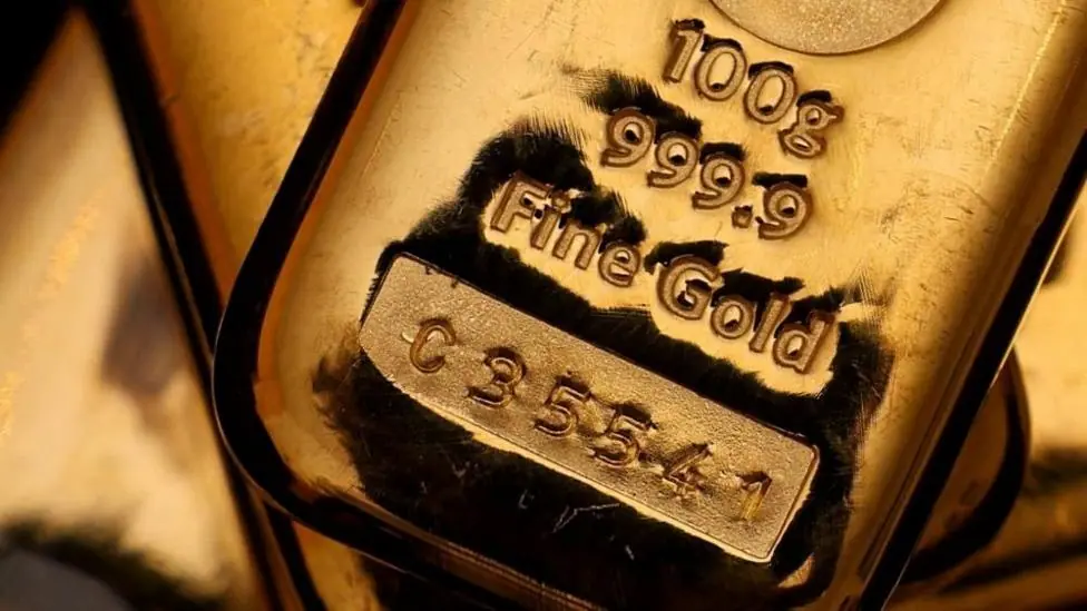 A shining gold bar with "100g, 999.9 fine gold, C 3 5 5 4 1" stamped into it.