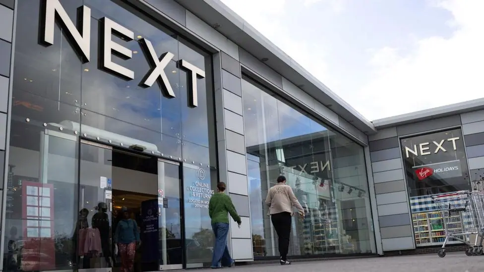 A Next store is seen with the logo looming large over passers-by as they walk outside the storefront on a sunny-cloudy day in Basildon in October.