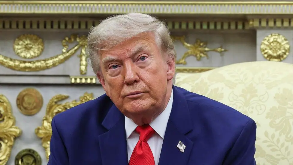 President Donald Trump. He has a serious look on his face and is wearing a blue suit with a white shirt and red tie.