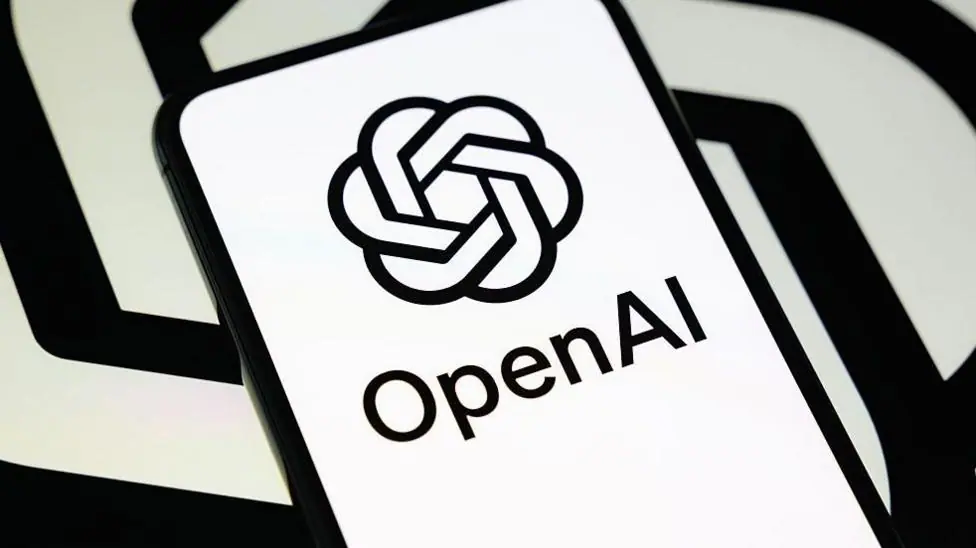 OpenAI's logo in black and white on a phone against a black and white spiral backdrop like its logo