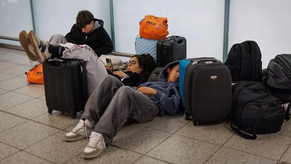 People laying on the floor in an airport with bags around them.