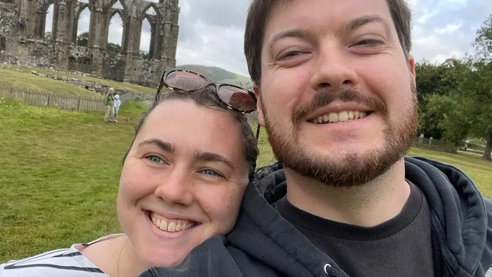 Selfie of a smiling Catie and Phil Allen standing in front of some ruins.