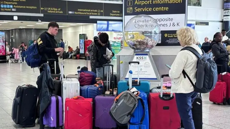 A group of people stand around a collection of suitcases and luggage at Gatwick Airport