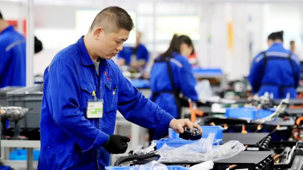 Workers in blue overalls assemble batteries for electric vehicles at a Chinese battery plant.