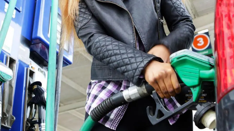 Person wearing a black leather jacket filling up their car from the petrol pump