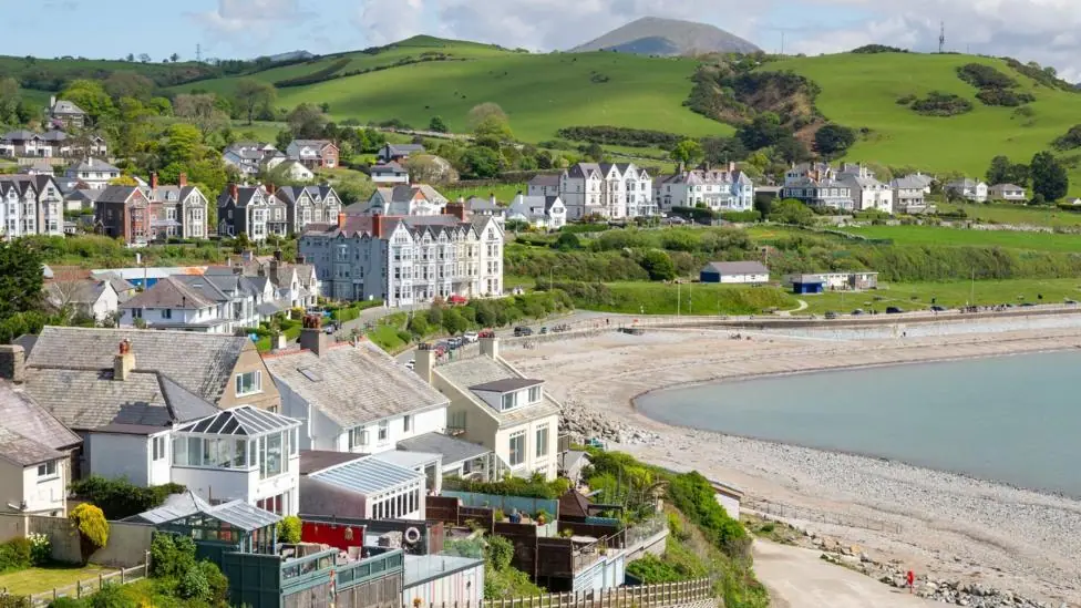 General view of the seaside town of Criccieth in north Wales, including a pebble beach and large townhouses overlooking the seafront, in the sunshine.