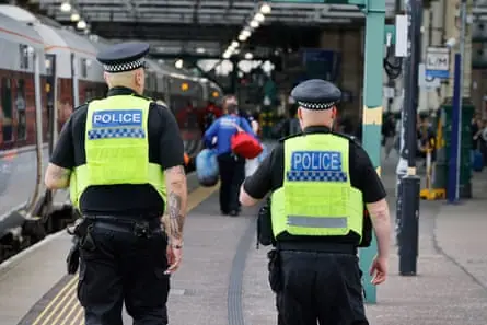 Two transport police in hi-vis jackets walking down a rail platform next to train.