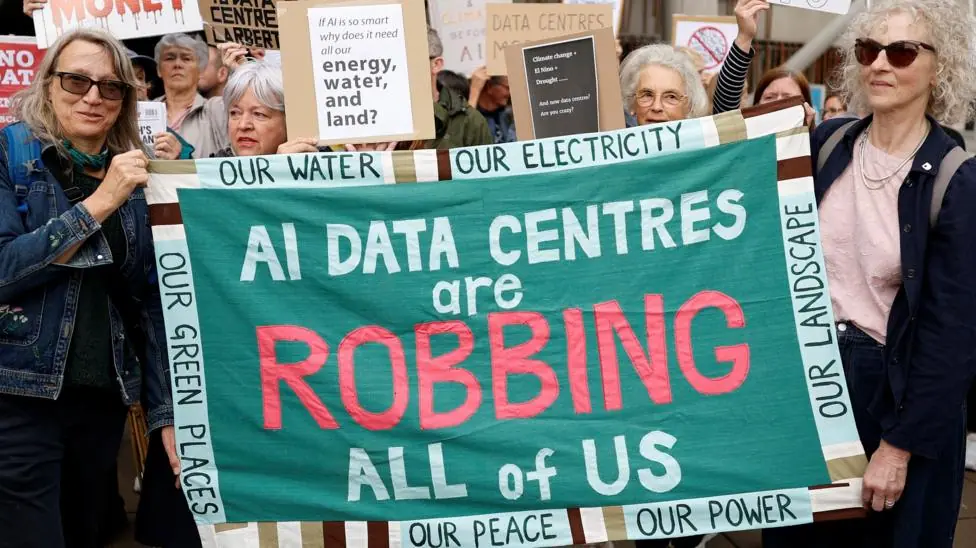 Activists protesting against data centres in their local area outside the Scottish parliament. Two women are holding a banner which reads: "AI DATA CENTRES ARE ROBBING ALL OF US".
