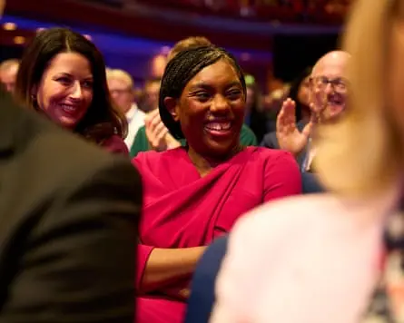 Badenoch smiles in the audience of Andrew Griffith's speech at the conference