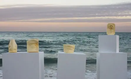 Body parts carved out of butter, on plinths, by the ocean