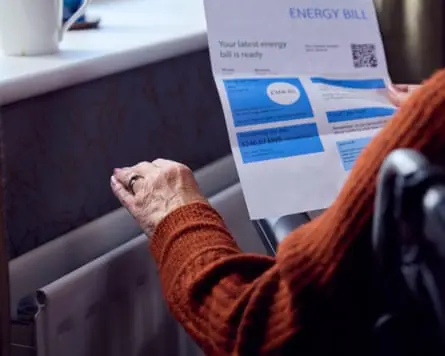 Someone sitting by a radiator holding an energy bill
