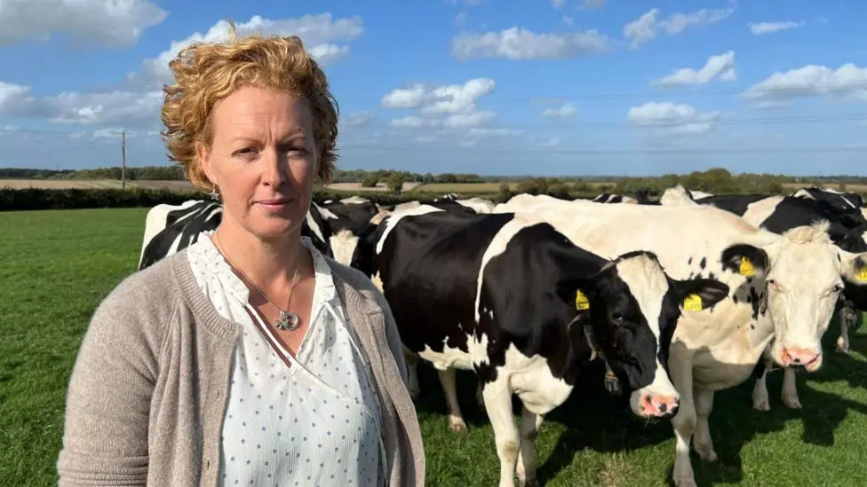 A woman stood in a field with about five cows behind her.