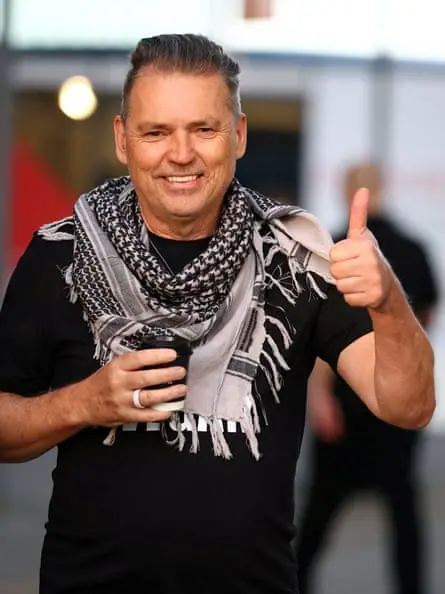 Wearing a black T-shirt and a grey and black scarf, Dale Vince gives a photographer a thumbs-up
