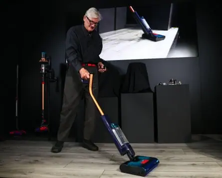 On an illuminated stage, Sir James Dyson demonstrates one of his vacuum cleaners