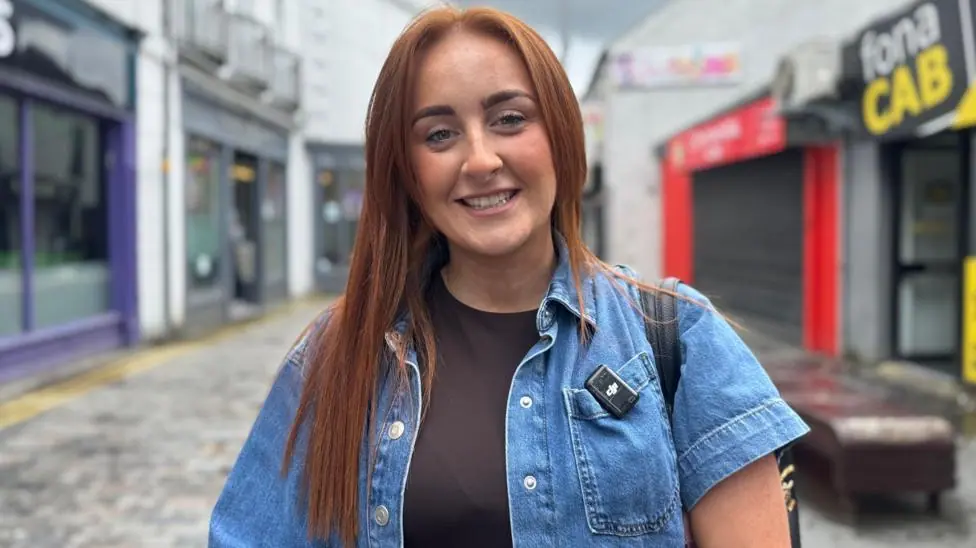 A woman with with dark hair, she has a denim jacket and dark top on
