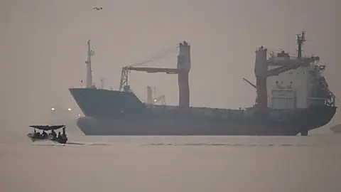 A motorboat passes an anchored cargo ship in the Strait of Hormuz off Bandar Abbas, Iran, early Monday, Sept. 28, 2026.