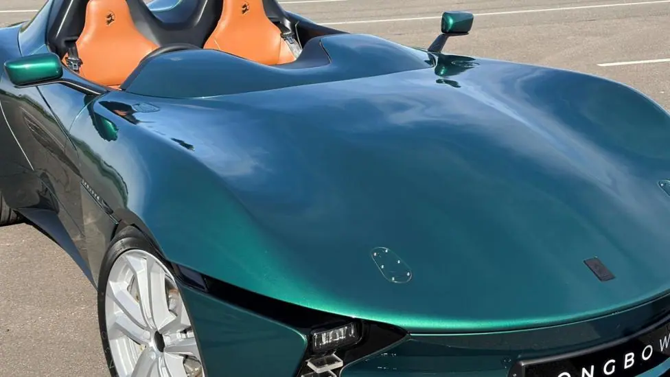 The front of a long, blue sports car, with part of a number plate reading ‘Longbow’ visible.