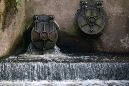 Water discharges from an outlet pipe into a river
