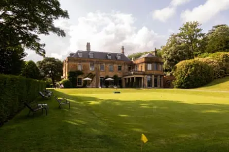 A historic stone building is seen across a green croquet lawn.