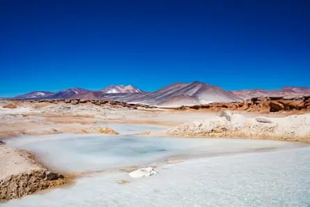 Salt flats mingle with the red rocks of the Atacama desert, under a deep blue sky.