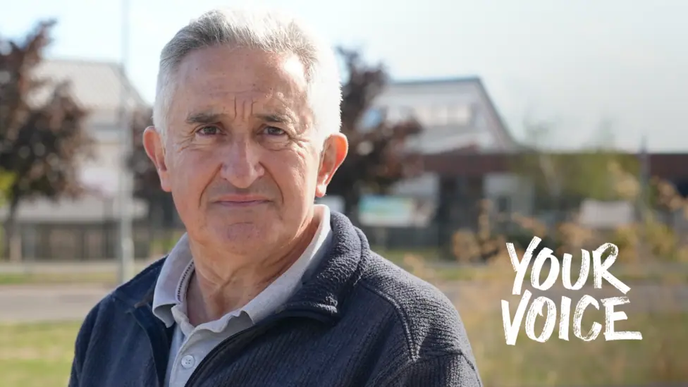 Bryn Dymott, wearing a polo shirt and cardigan, standing on grass in front of some buildings blurred in the background. The words "Your Voice" are imposes on the photo on the left.