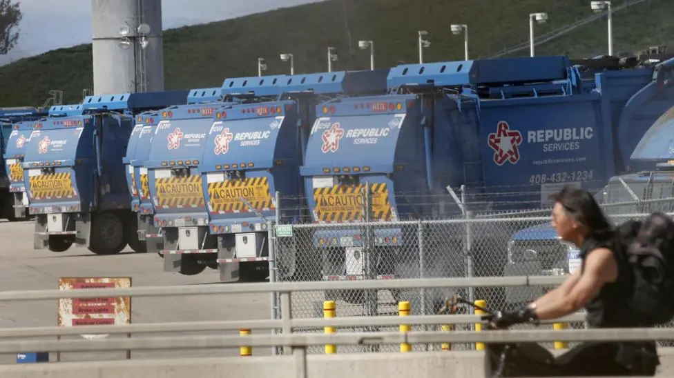 Blue rubbish trucks lined up at Newby Island landfill. A cyclist is in the foreground.