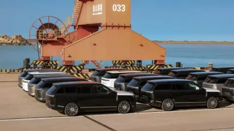 Xpeng GX SUVs lined up beneath an orange dockside crane.