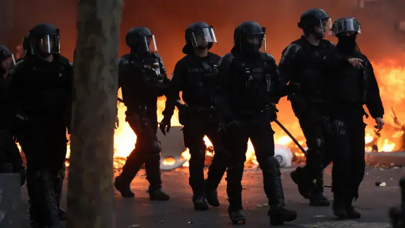 巴黎防暴警察在示威日與抗議者爆發衝突期間，走過一道燃燒中的路障（17/10/2026）