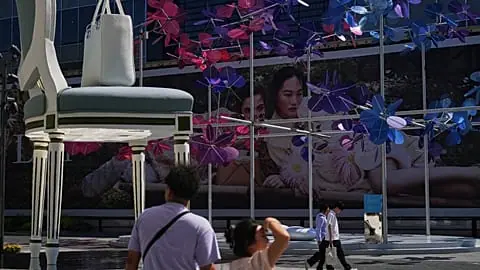 File - Shoppers walk by a giant chair and a handbag on display at a luxury outdoor shopping mall decorated with flower shaped fans in Beijing, Thursday, 3 Sept. 2026.