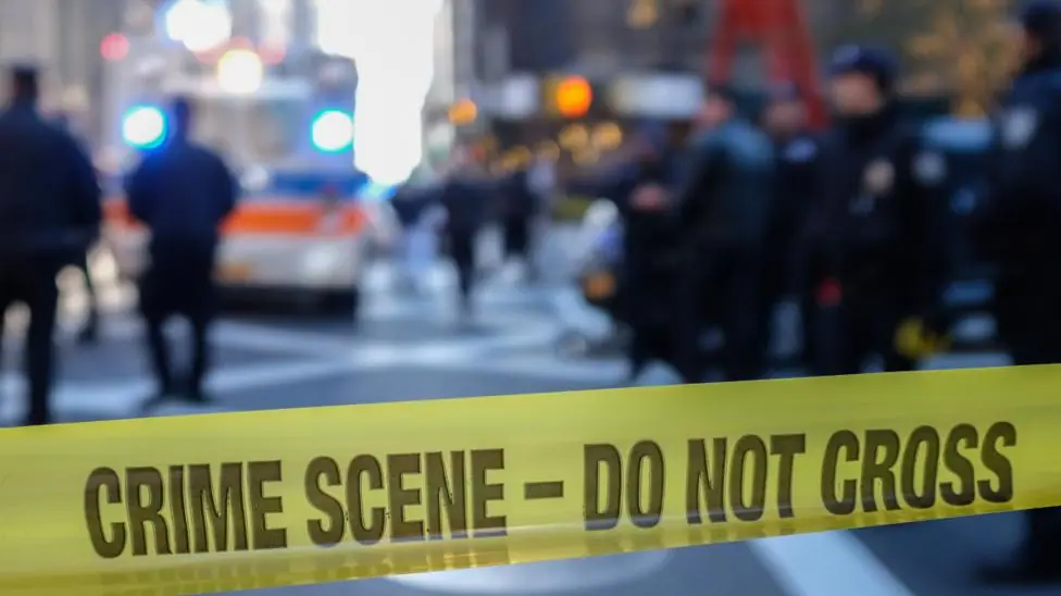 Police sealing off a US city street with yellow tape reading "crime scene - do not cross".