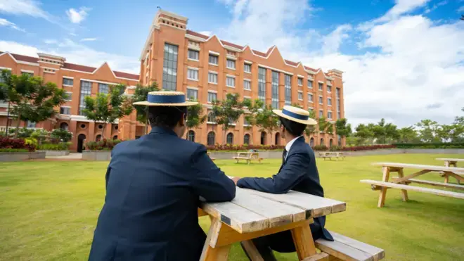 班加羅爾哈羅學校的學生們坐在花園裡，穿著傳統制服和帽子，望著主樓。