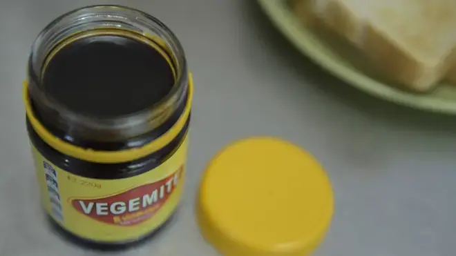 一瓶Vegemite醬放在桌上，旁邊有一片多士。