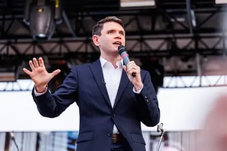 James Talarico, a man in a blue suit jacket, stands on stage and speaks into microphone with hand gestured