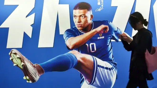 Pedestrians pass by an electrolyte drink advertisement for French football player Kylian Mbappé in the subway in Shanghai, China on June 30, 2026